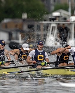 Joshua racing in a Cal crew boat, mid-stroke with spray